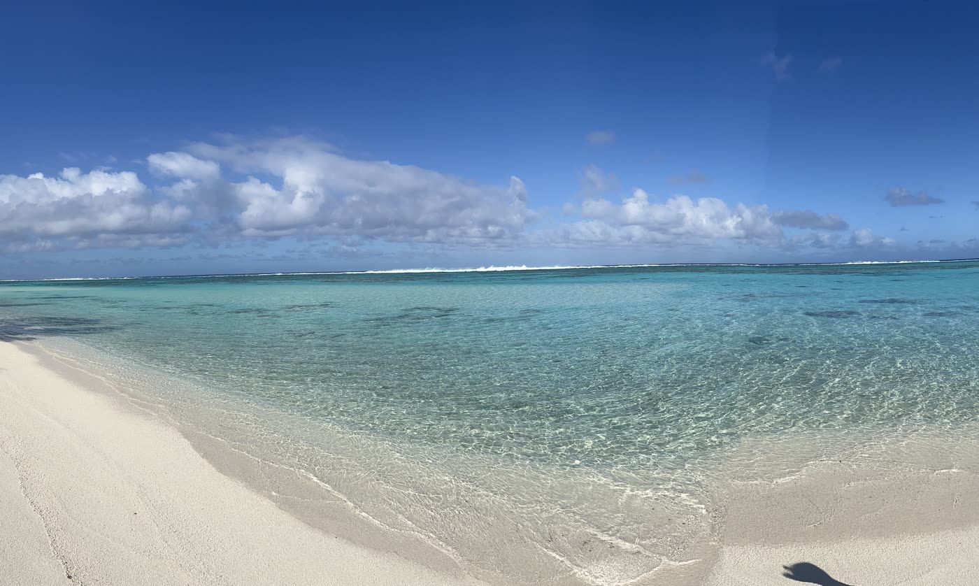 A wide white-sand beach curving along a pale turquoise lagoon