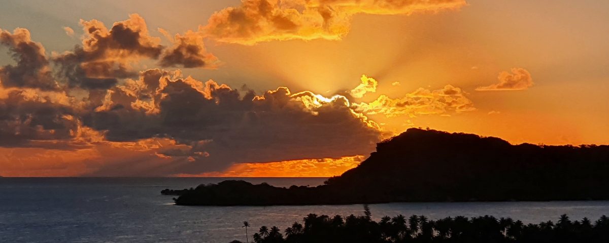 Sunset over Bora Bora’s lagoon, with a palm-covered headland in silhouette