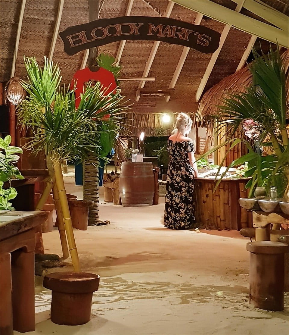 The sand-floored dining room at Bloody Mary’s under its thatched roof and carved sign